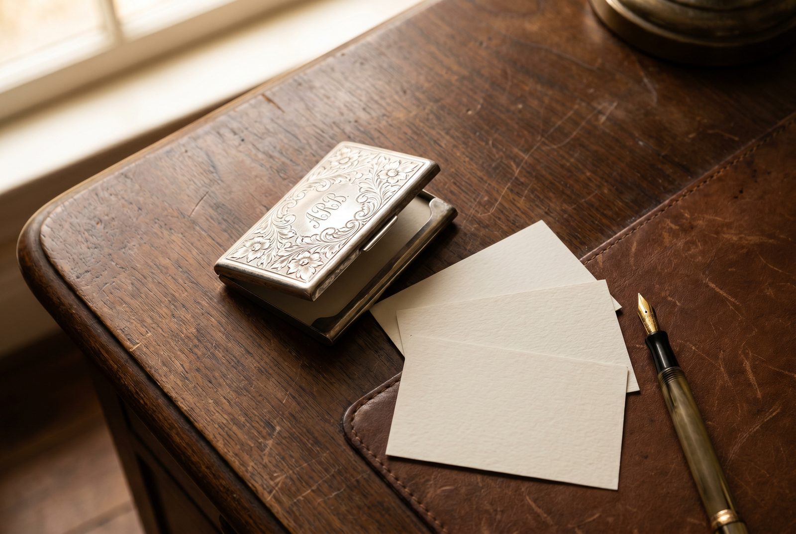 An antique silver card case with calling cards and a fountain pen on a desk