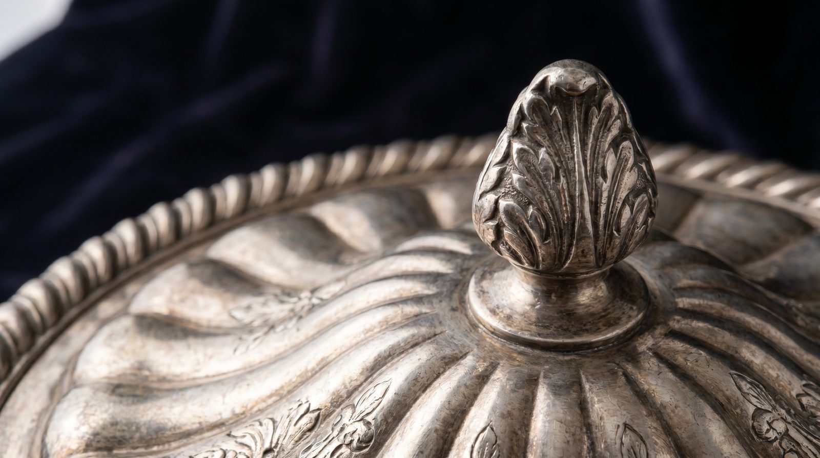 Cast finial and gadrooned rim of an antique silver soup tureen cover