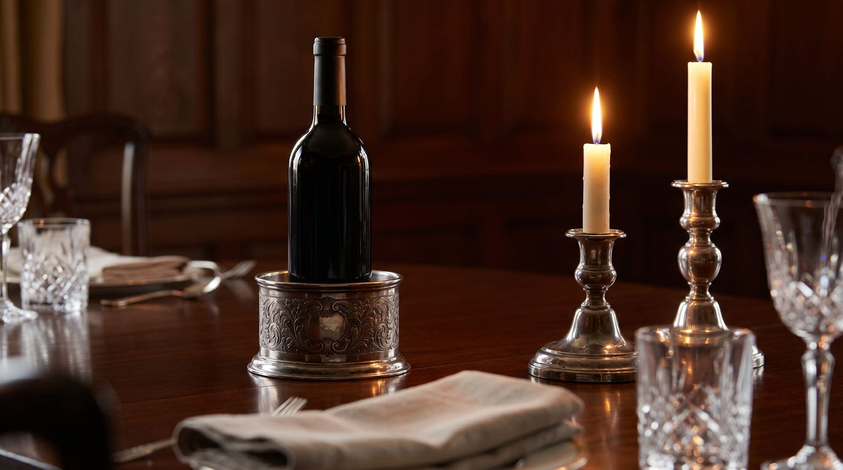 Antique silver wine coaster holding a wine bottle on a dining table