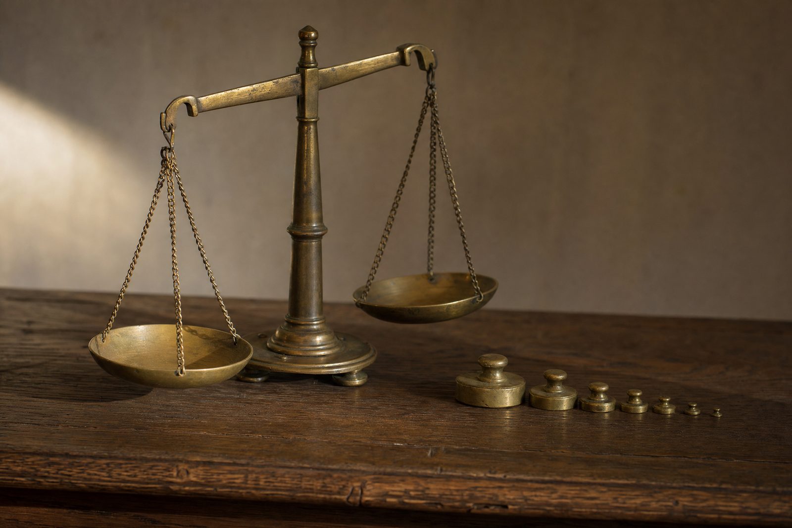 Antique brass balance scale with empty pans and a graduated stack of brass weights on dark oak