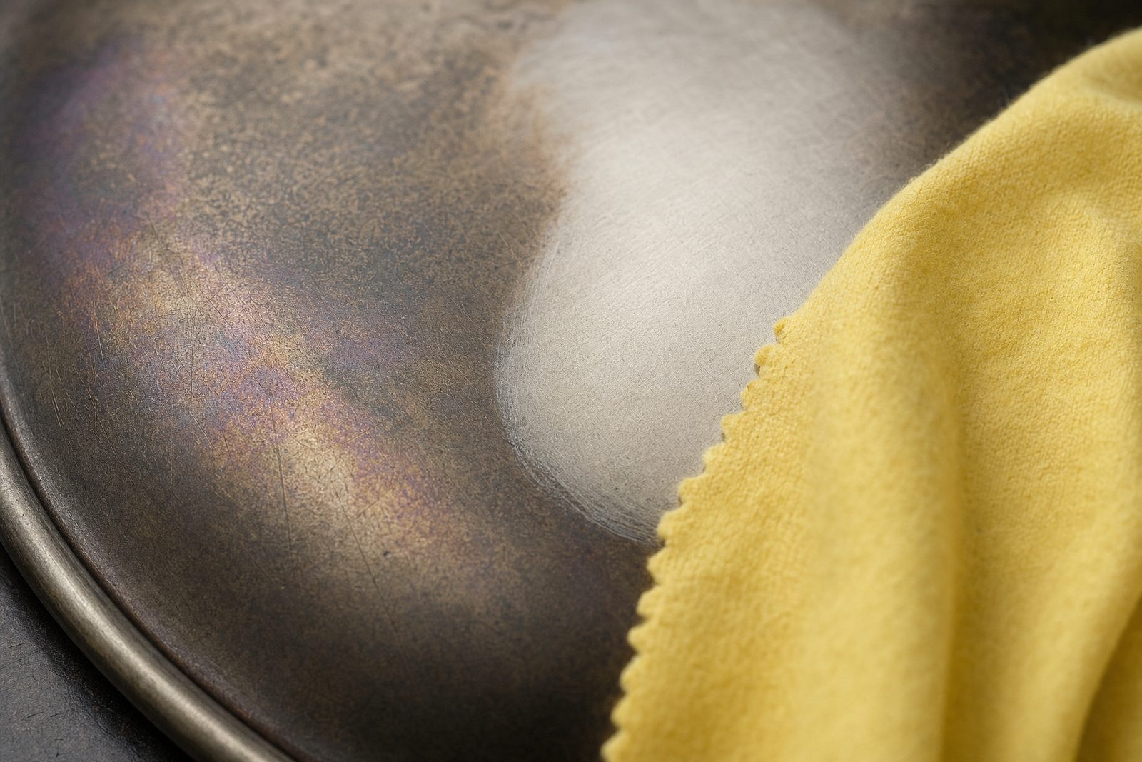 Close-up of tarnished antique silver with one area rubbed back to a sheen by a yellow polishing cloth
