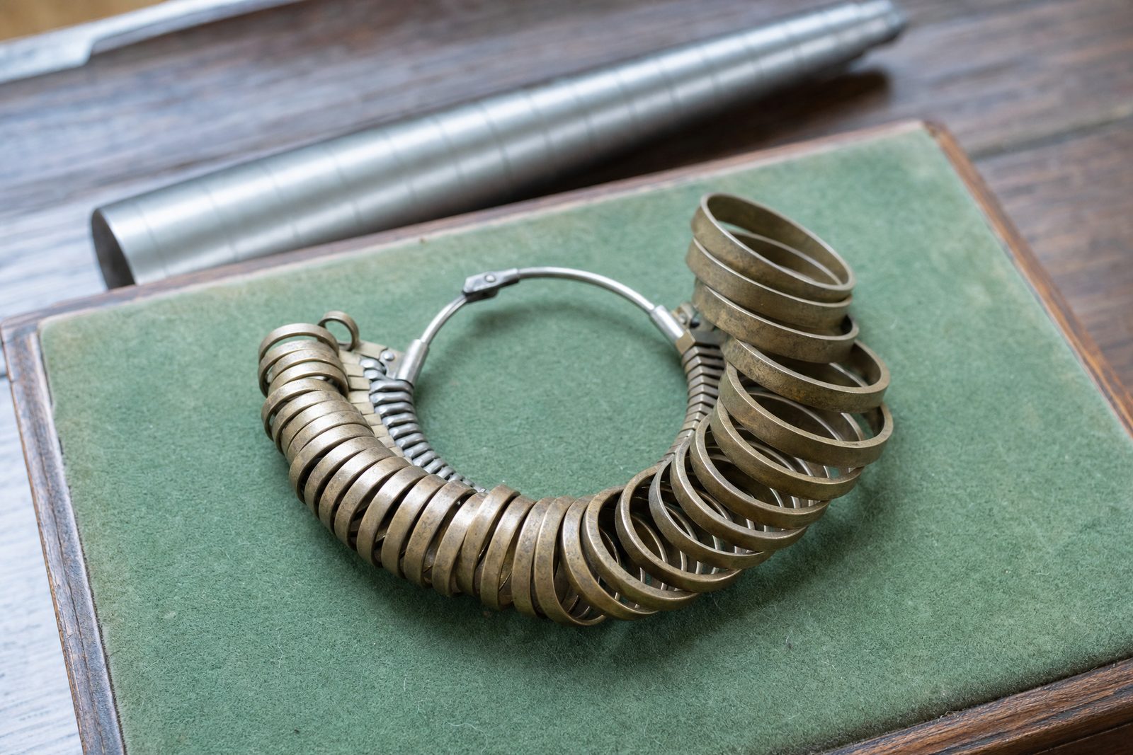 Set of antique brass ring-size gauges fanned open on green baize beside a steel sizing stick