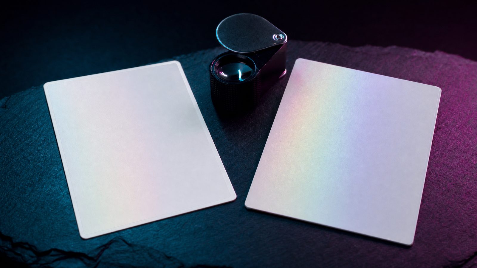 Two trading cards side by side on a dark desk under a loupe, one Japanese and one English, showing border and centring differences