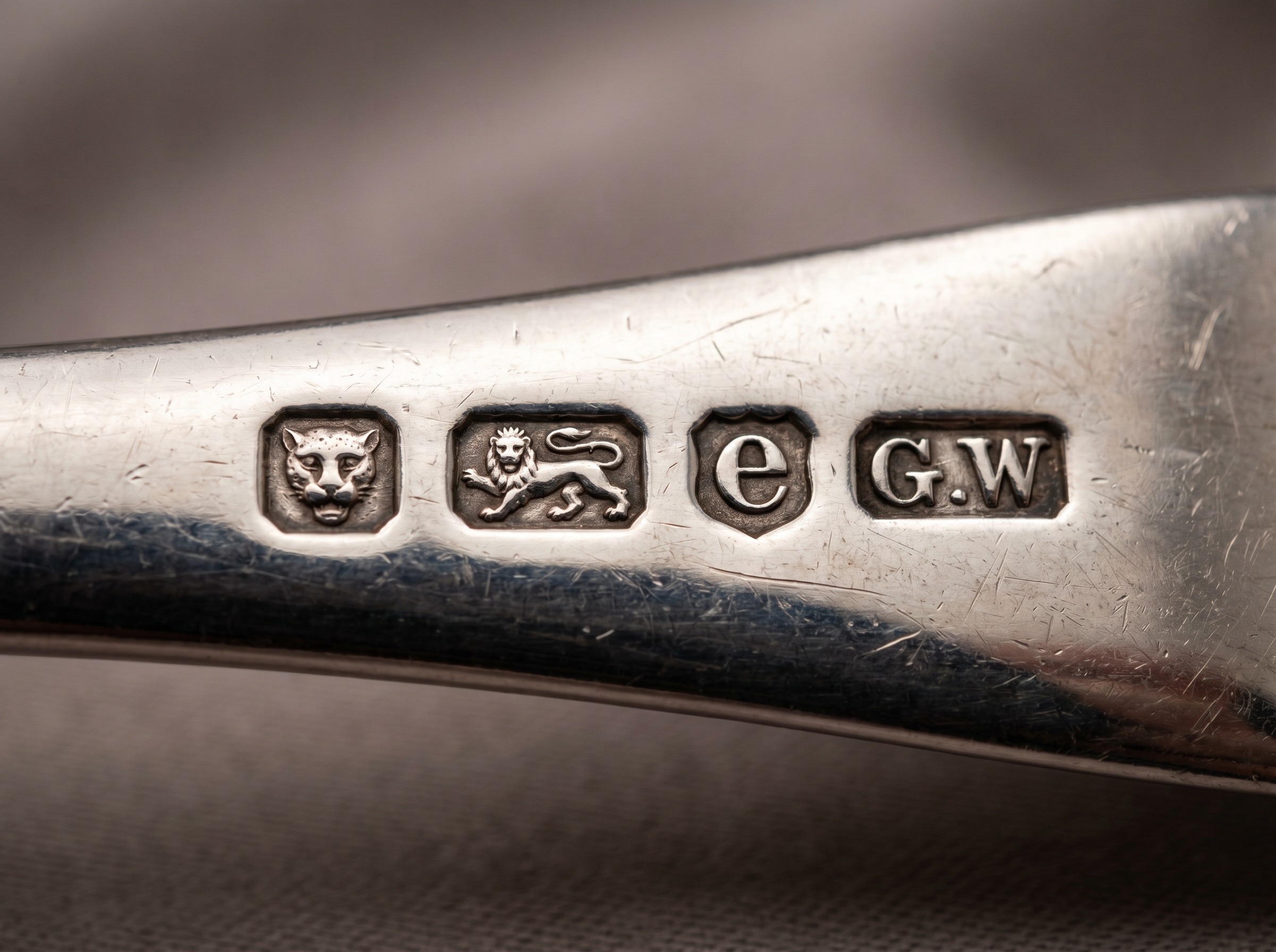 Extreme macro of a full Chester hallmark row on antique sterling silver — wheatsheaves, lion passant, date letter and maker's mark