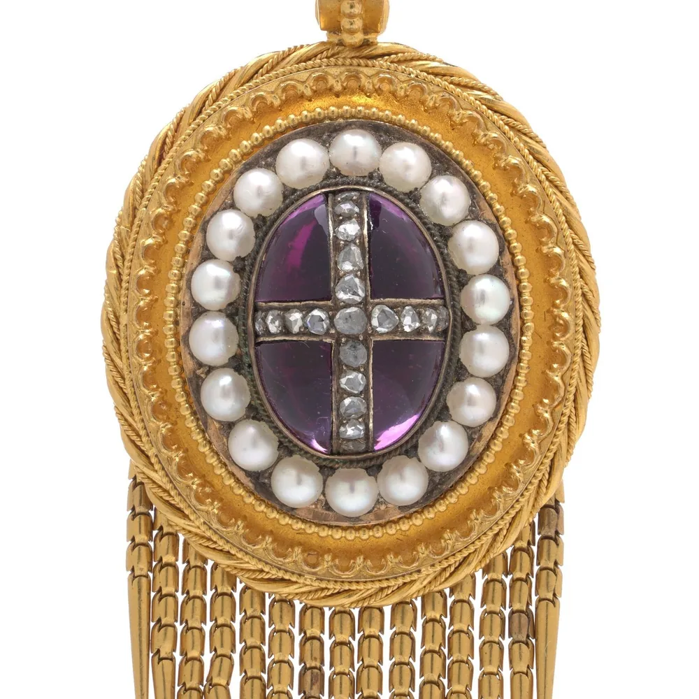 Close-up of a Victorian 21KT gold pendant: a cabochon amethyst with a rose diamond cross, a frame of pearls and a rope-twist gold border