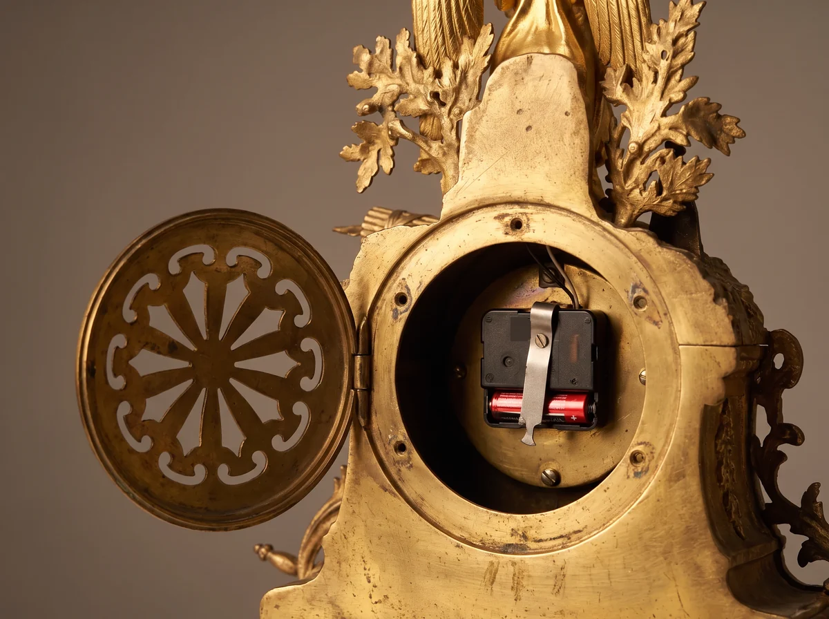 Back of an antique gilt mantel clock with the back door open, showing a modern plastic battery quartz unit fitted where the original brass movement was