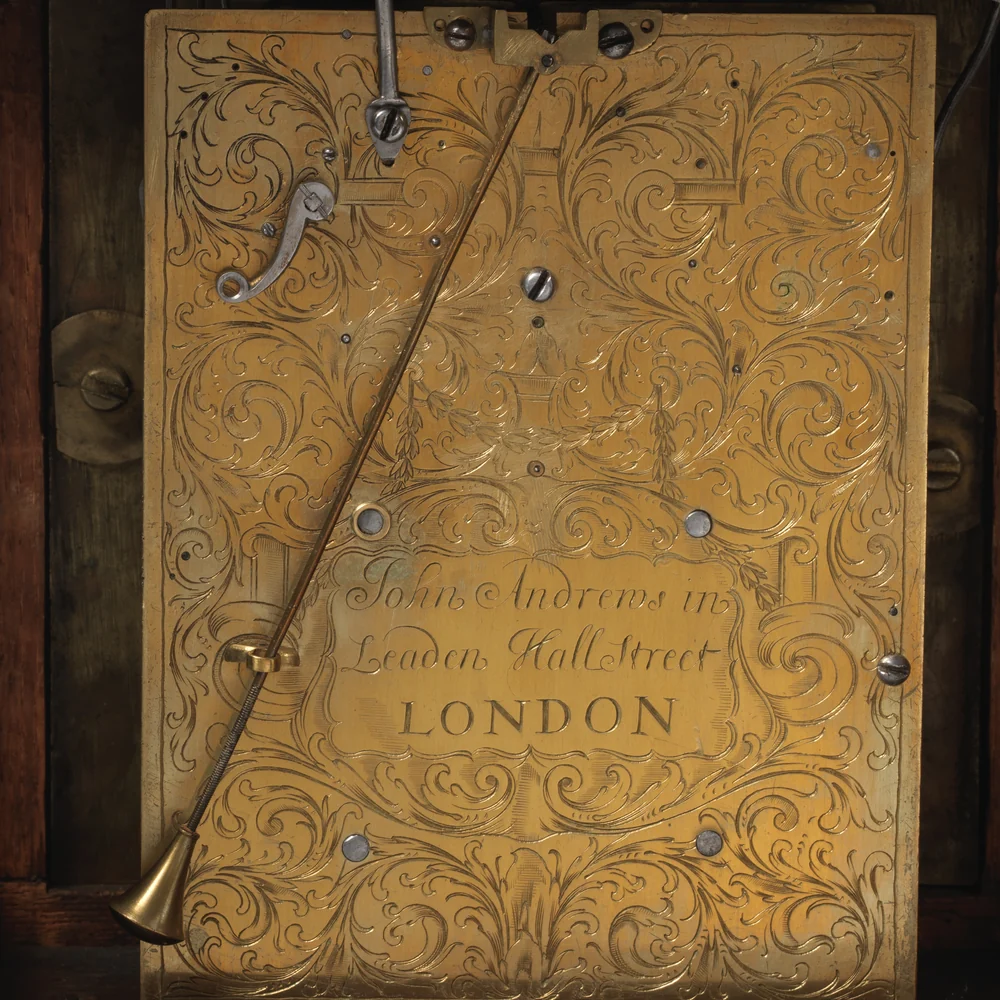 Engraved brass backplate of a 1690 English bracket clock signed John Andrews in Leaden Hall Street London, with the pendulum hanging in front