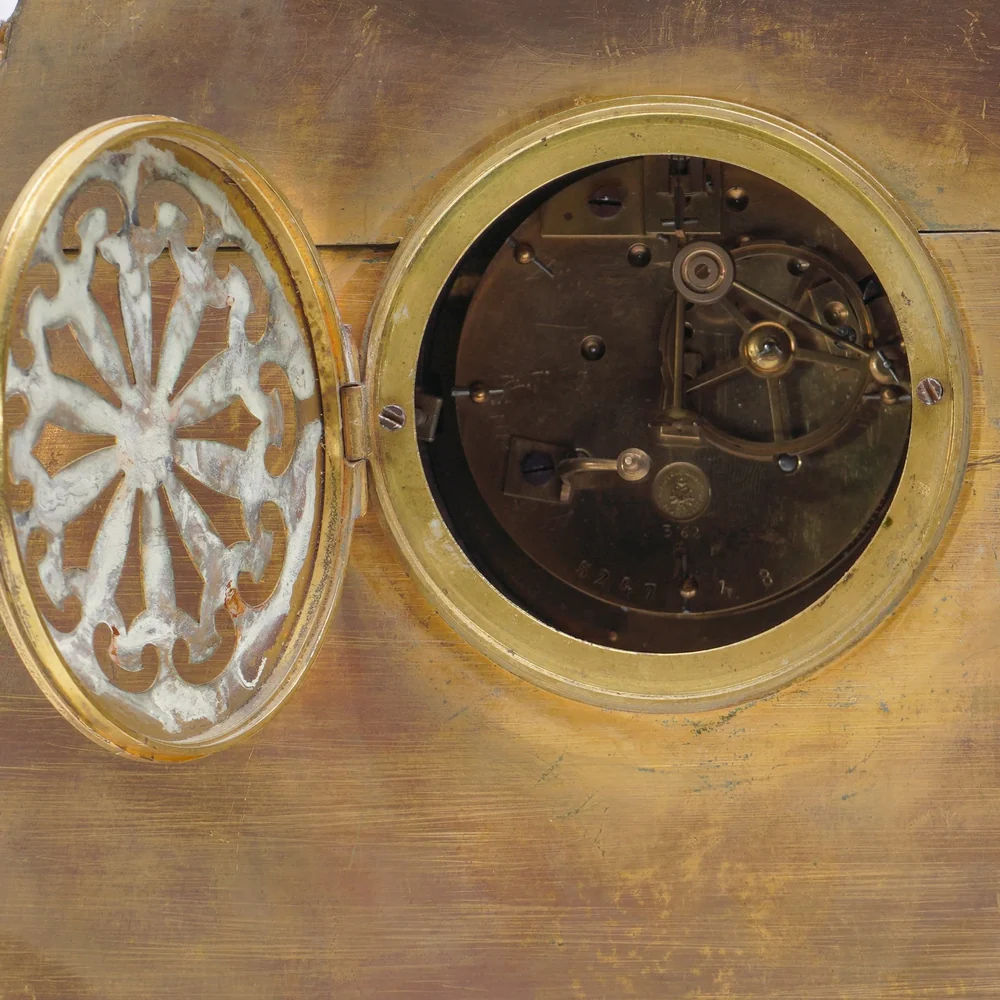 Round French clock movement seen through the open back door of a gilt bronze mantel clock, showing the backplate, stamp and pendulum crutch