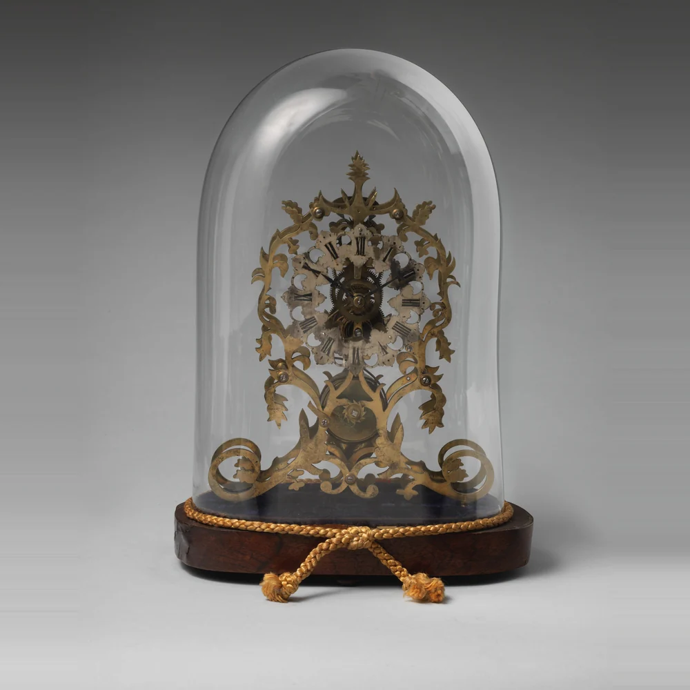 Victorian brass skeleton clock of about 1850 to 1865 with a pierced scrolling frame under a glass dome on a wooden base