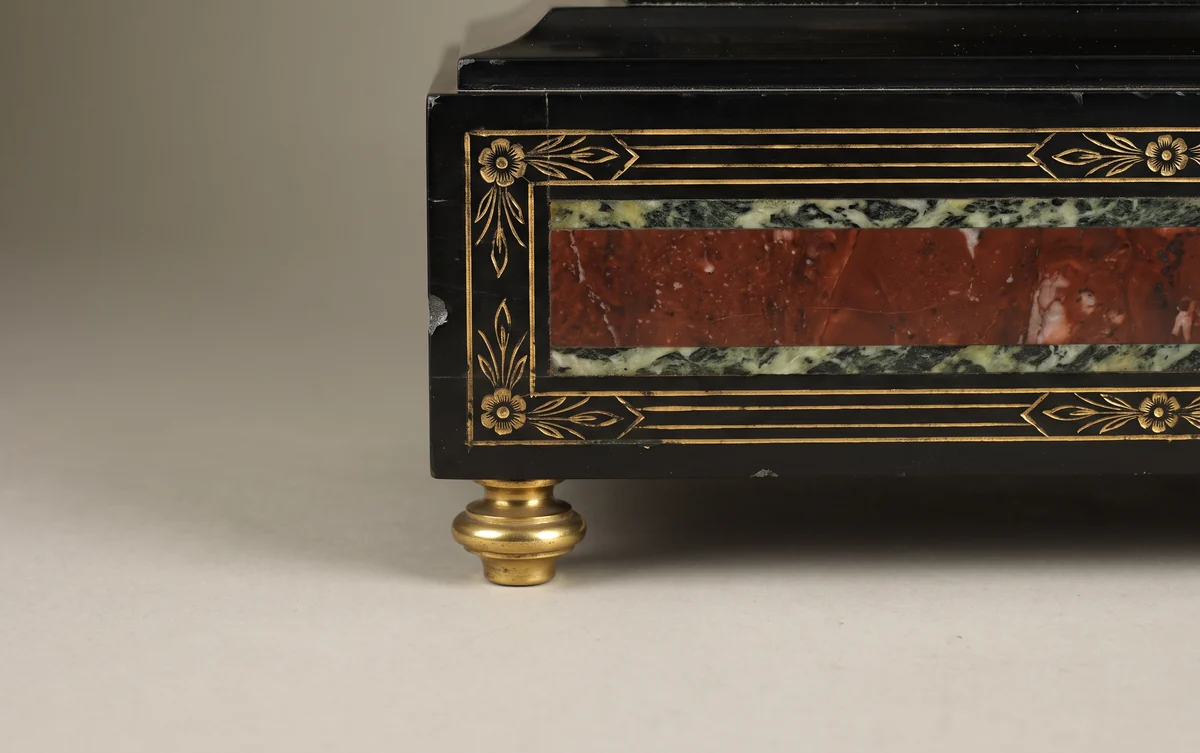 Corner of a black slate mantel clock case with inset red and green marble bands, gilt incised decoration and a turned brass foot