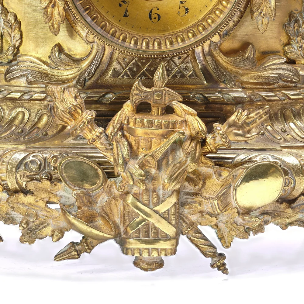 Gilt bronze trophy of arms mount with crossed swords and torches on the base of a French mantel clock, showing crisp casting and rubbed high points