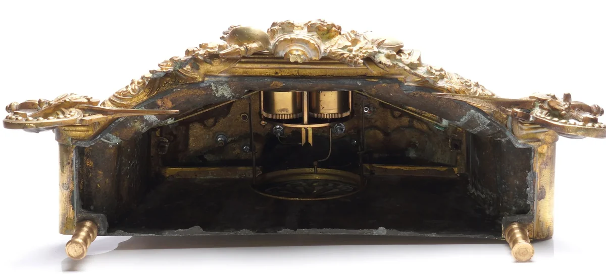 Underside of a French gilt bronze mantel clock showing the yellow bare metal inside the case and the bottom of the movement