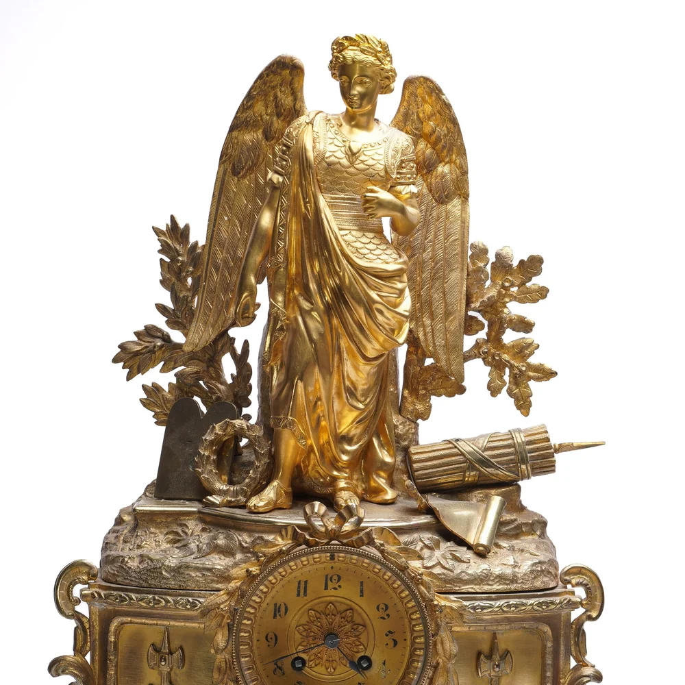 Winged gilt bronze figure holding a wreath above the dial of a 19th century French mantel clock, framed by oak leaves