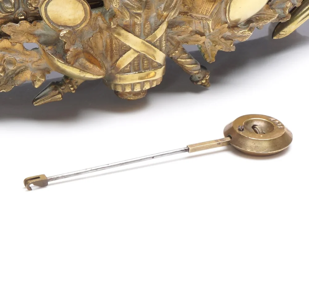 Brass pendulum with a round bob and hooked rod from a French mantel clock, lying beneath the gilt bronze base