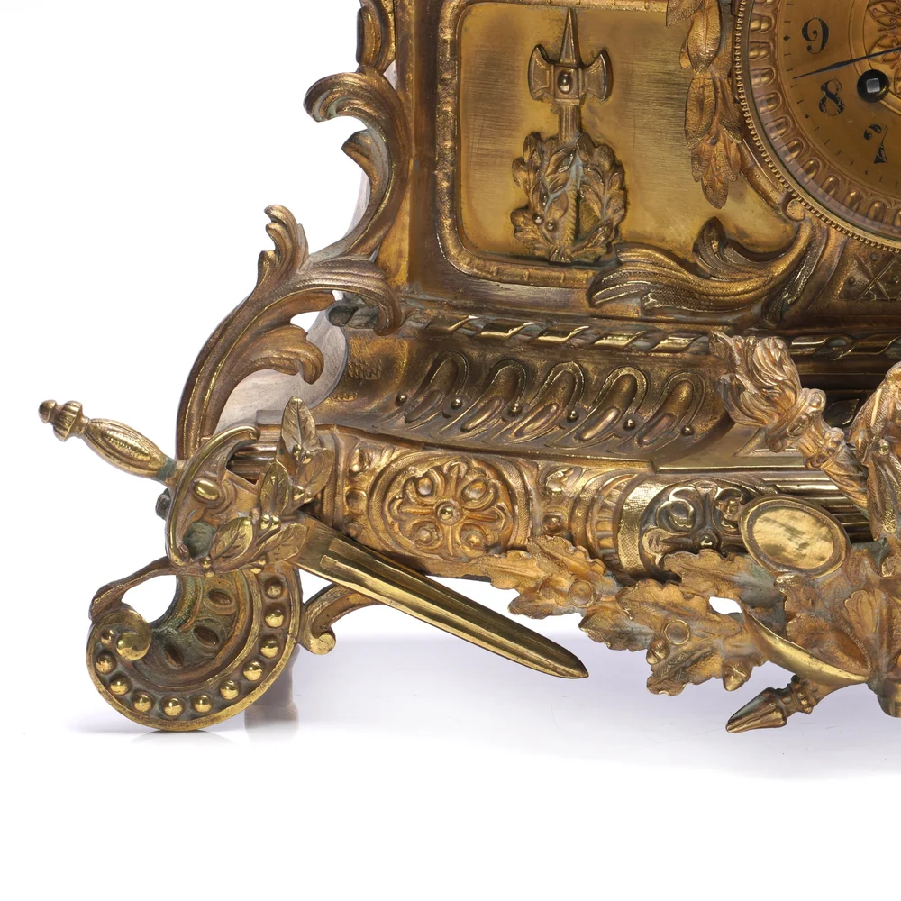Scrolled rococo revival foot and trophy mounts on the base of a 19th century French gilt bronze mantel clock