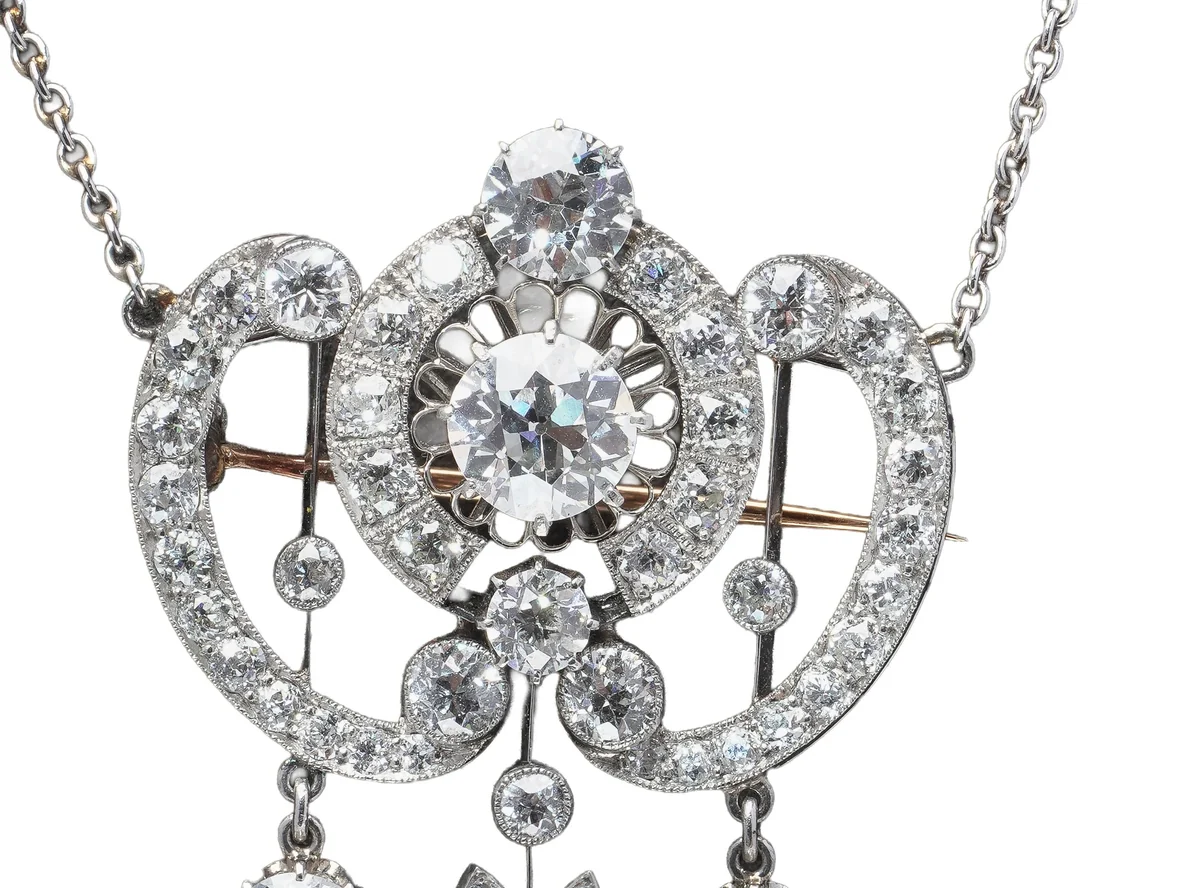 An Edwardian platinum and diamond pendant brooch: two opposed garland scrolls of graduated old cut diamonds around a large old European cut centre