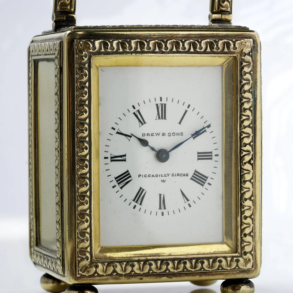 White enamel carriage clock dial signed Drew and Sons, Piccadilly Circus, the London retailer, with Roman numerals and blued hands