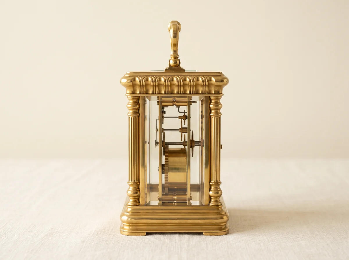 Carriage clock movement seen edge-on through the bevelled side glass, between gilt corner pillars