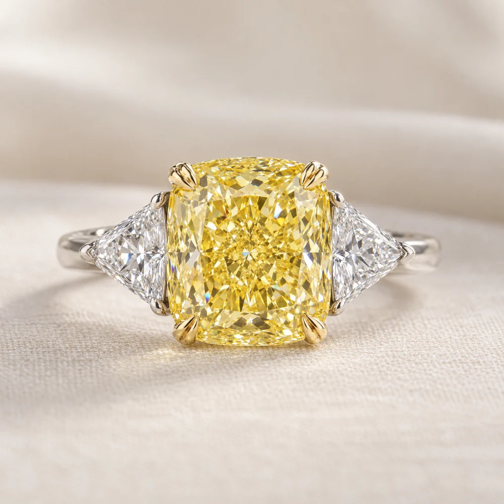 Illustration of a three stone ring: a yellow cushion cut diamond in yellow gold claws between two colourless trillion cut diamonds on a platinum band