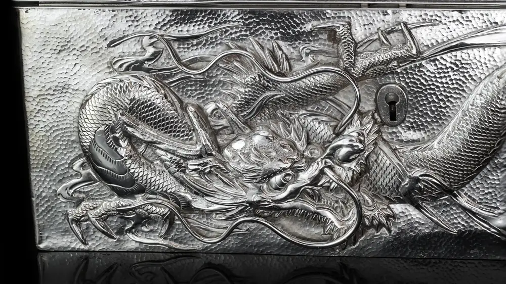 Close-up of a deeply chased dragon on the front of a Chinese export silver box, with the lock plate