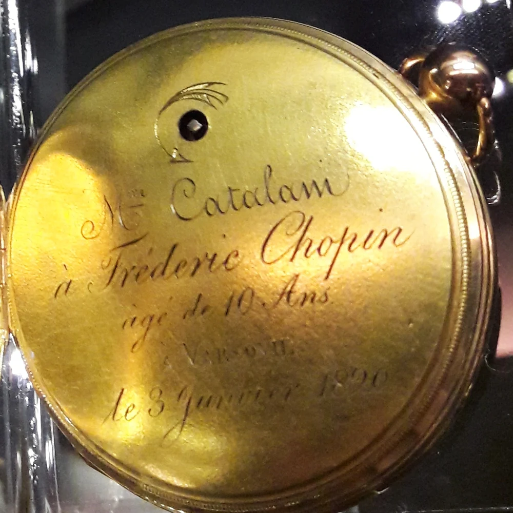 Chopin's gold pocket watch open in a museum case, the inner cover engraved in French with a dedication from Madame Catalani dated 3 January 1820
