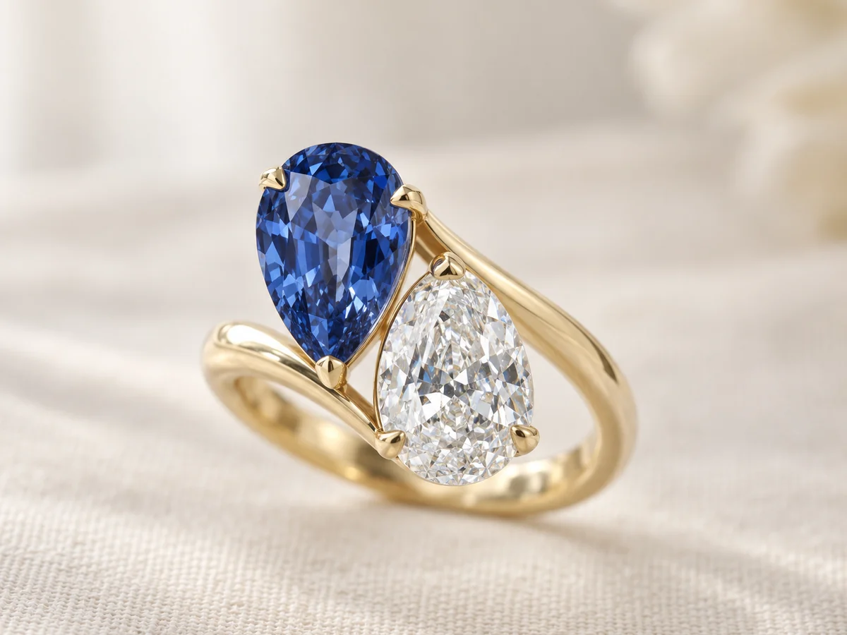 Illustration of a toi et moi ring with a pear-shaped blue sapphire and a pear-shaped diamond on a yellow gold crossover band