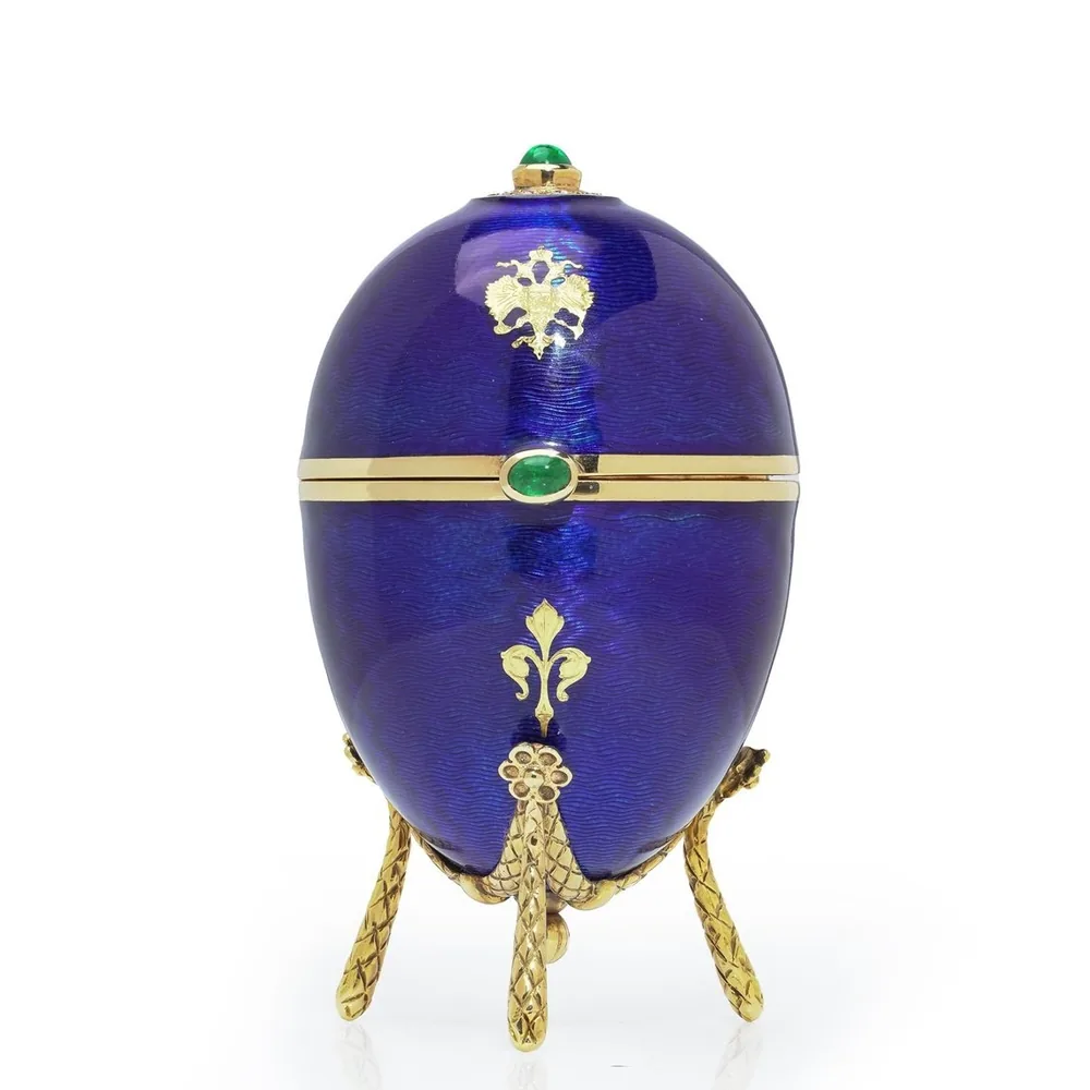 A modern Faberge egg in 18KT gold and royal blue guilloche enamel with cabochon emeralds on a tripod stand, numbered 6 of 25