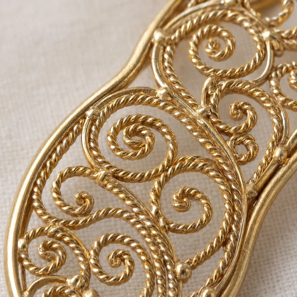 Macro of gold filigree: fine twisted and flattened wire bent into spirals and S-scrolls inside a plain gold frame