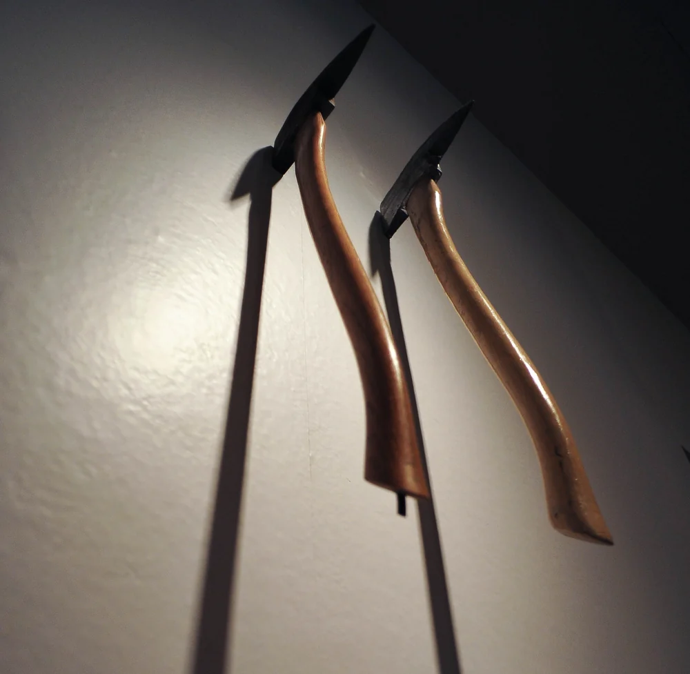 Two axes from The Shining hanging side by side on a gallery wall, with curved wooden handles and dark steel heads