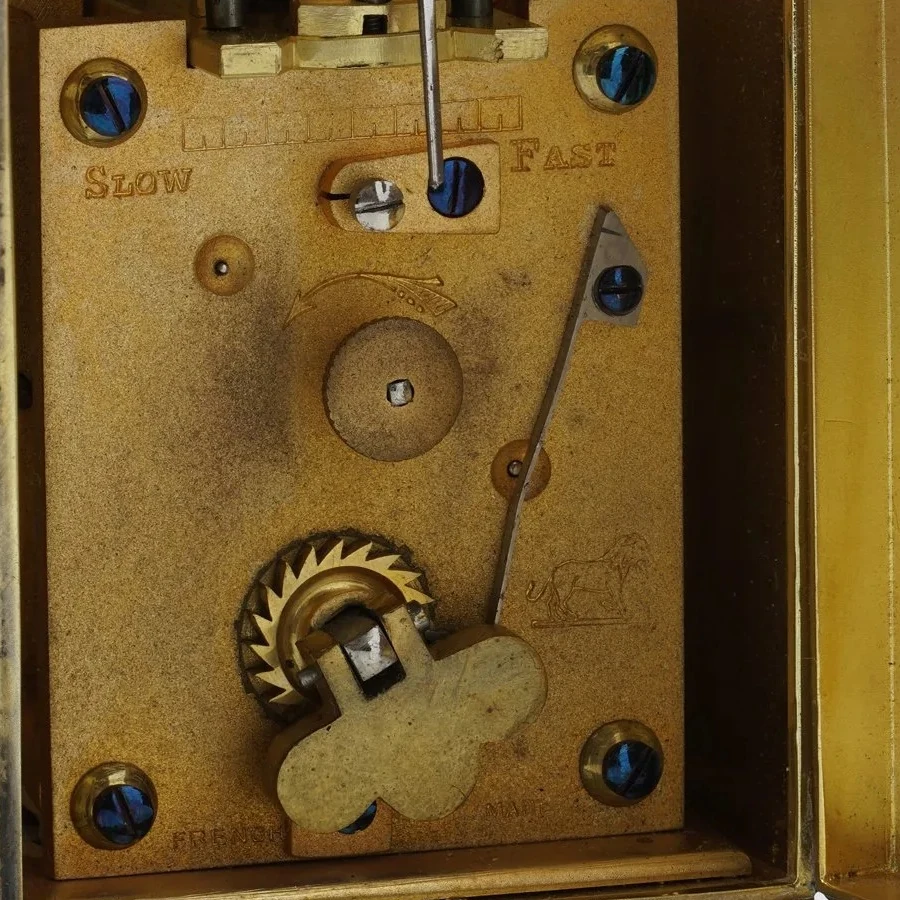 Gilt back plate of a French carriage clock movement stamped Slow and Fast, a lion trademark and French Made, with the winding key in place