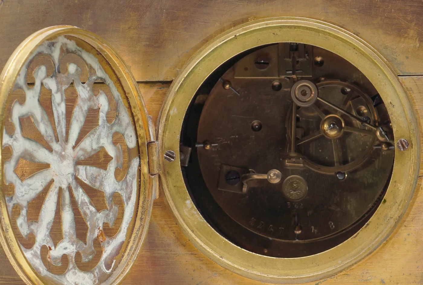 Open back door of a 19th century French gilt bronze mantel clock showing the round brass movement back plate with a small round maker's stamp and stamped numbers