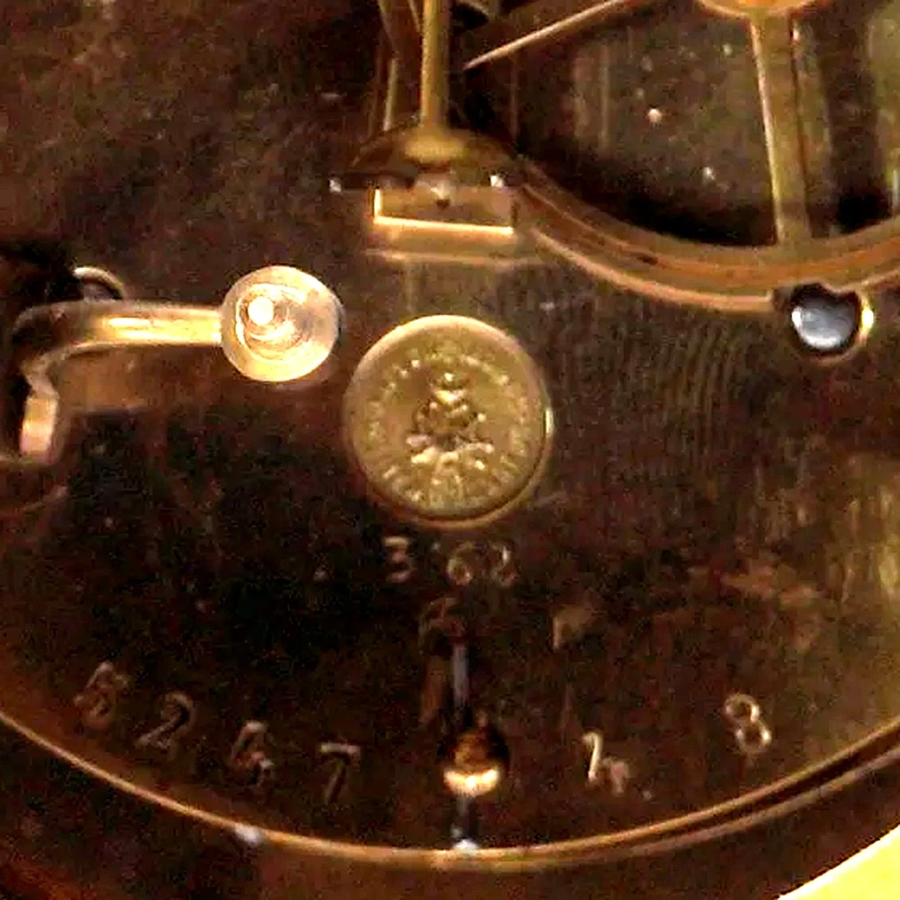 Close-up of a round medal-type stamp on a French clock movement back plate, with stamped numbers beneath it