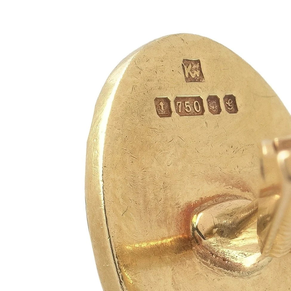 The back of a vintage 18ct gold cufflink with a sponsor's mark above a row of British hallmarks including 750 and the London leopard's head