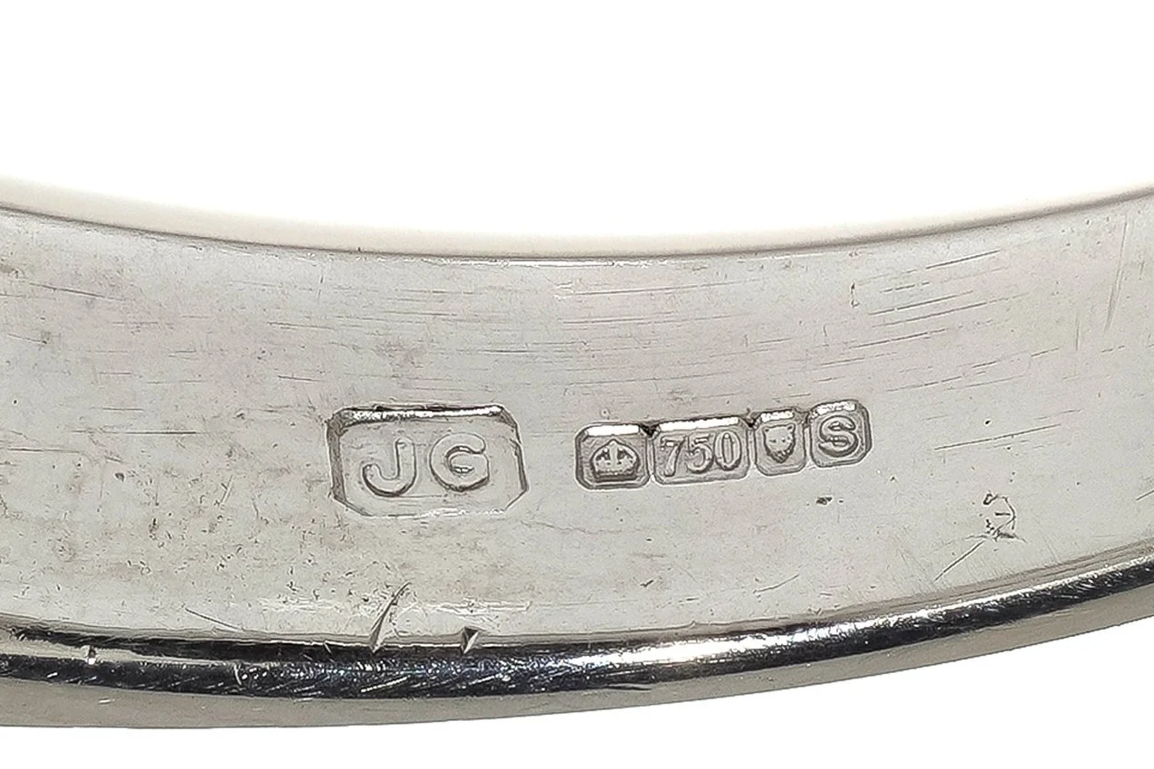 A full British hallmark inside the shank of an 18ct white gold ring: the JG sponsor's mark, a crown, 750 in its shield, the leopard's head of London and a date letter