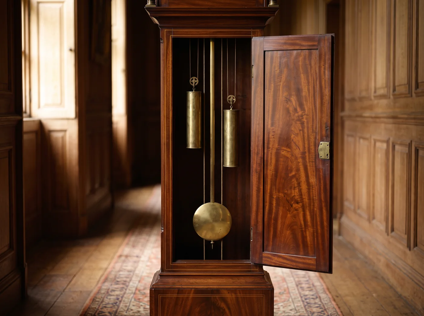 Antique mahogany longcase clock with its trunk door open, showing a brass pendulum bob and two brass-cased weights