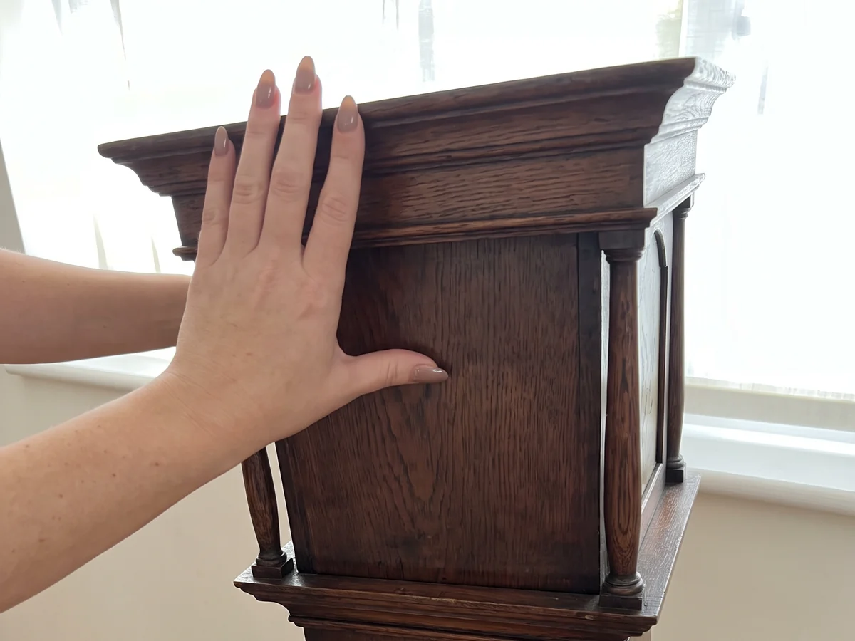 Hands easing the hood off an oak longcase clock, seen from the side