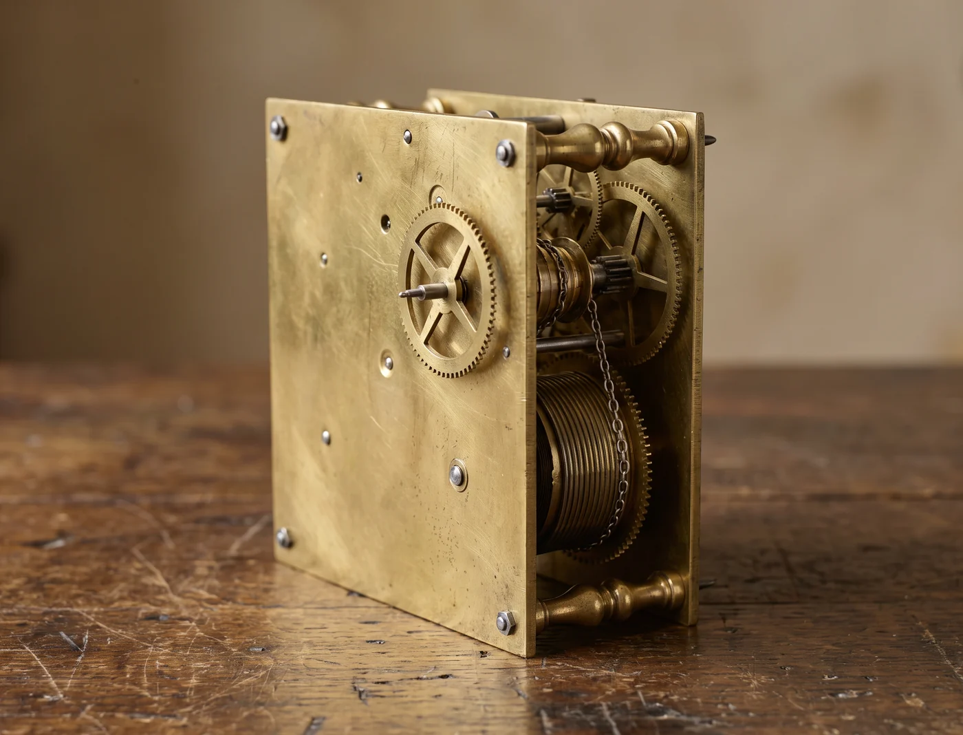 Antique English brass clock movement out of its case, showing the two brass plates joined by turned pillars, the wheels and the spring barrel