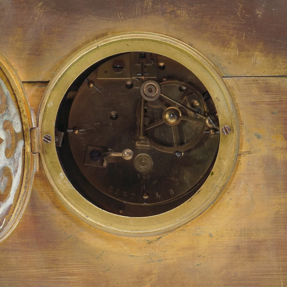 Back door open on a 19th century French gilt bronze mantel clock, showing the round brass movement with a circular maker's stamp and serial number