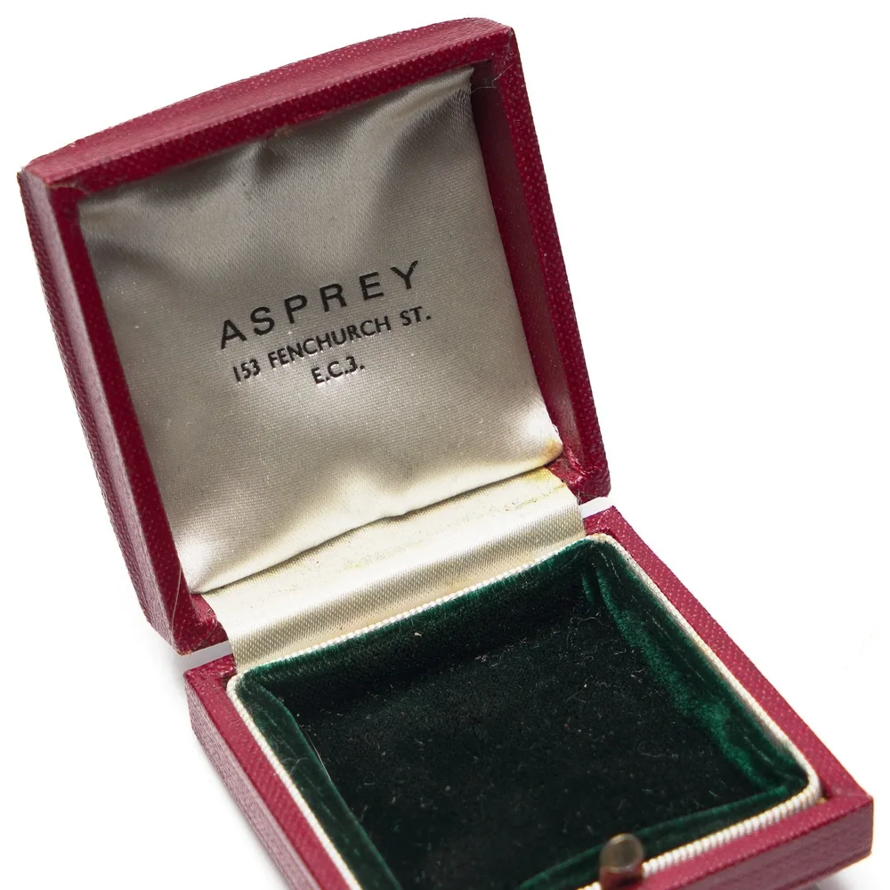 An Asprey red leather presentation box open to a grey satin lid printed Asprey, 153 Fenchurch St, E.C.3, with a green velvet base