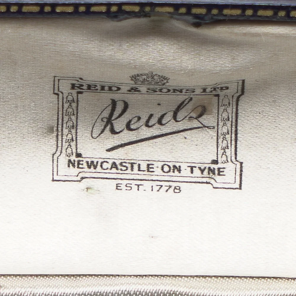 The white satin lid of a Reid & Sons Ltd brooch box printed with a crown, the Reids script signature, Newcastle on Tyne, Est. 1778