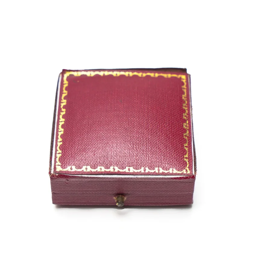 A closed red grained leather Asprey box with a gilt tooled border and a small brass push button catch at the front