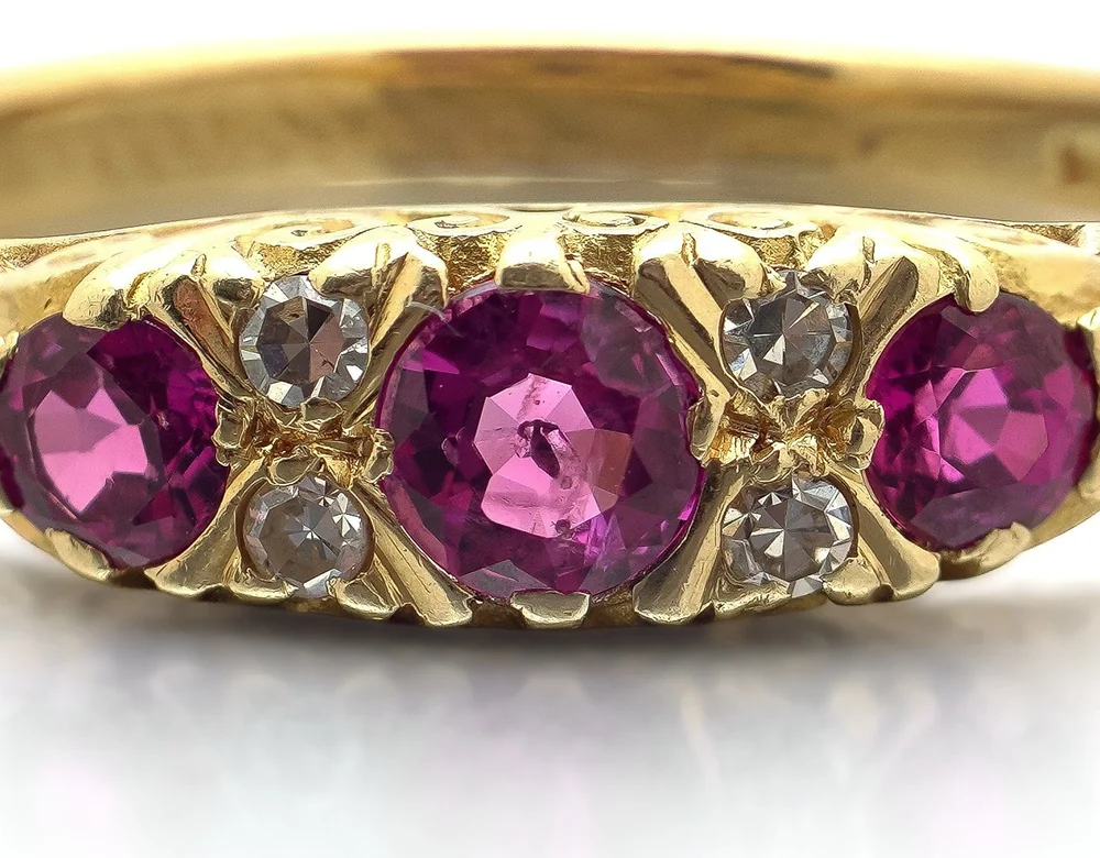 Close-up of the ruby half hoop ring: three round rubies divided by pairs of small diamonds in a carved yellow gold setting