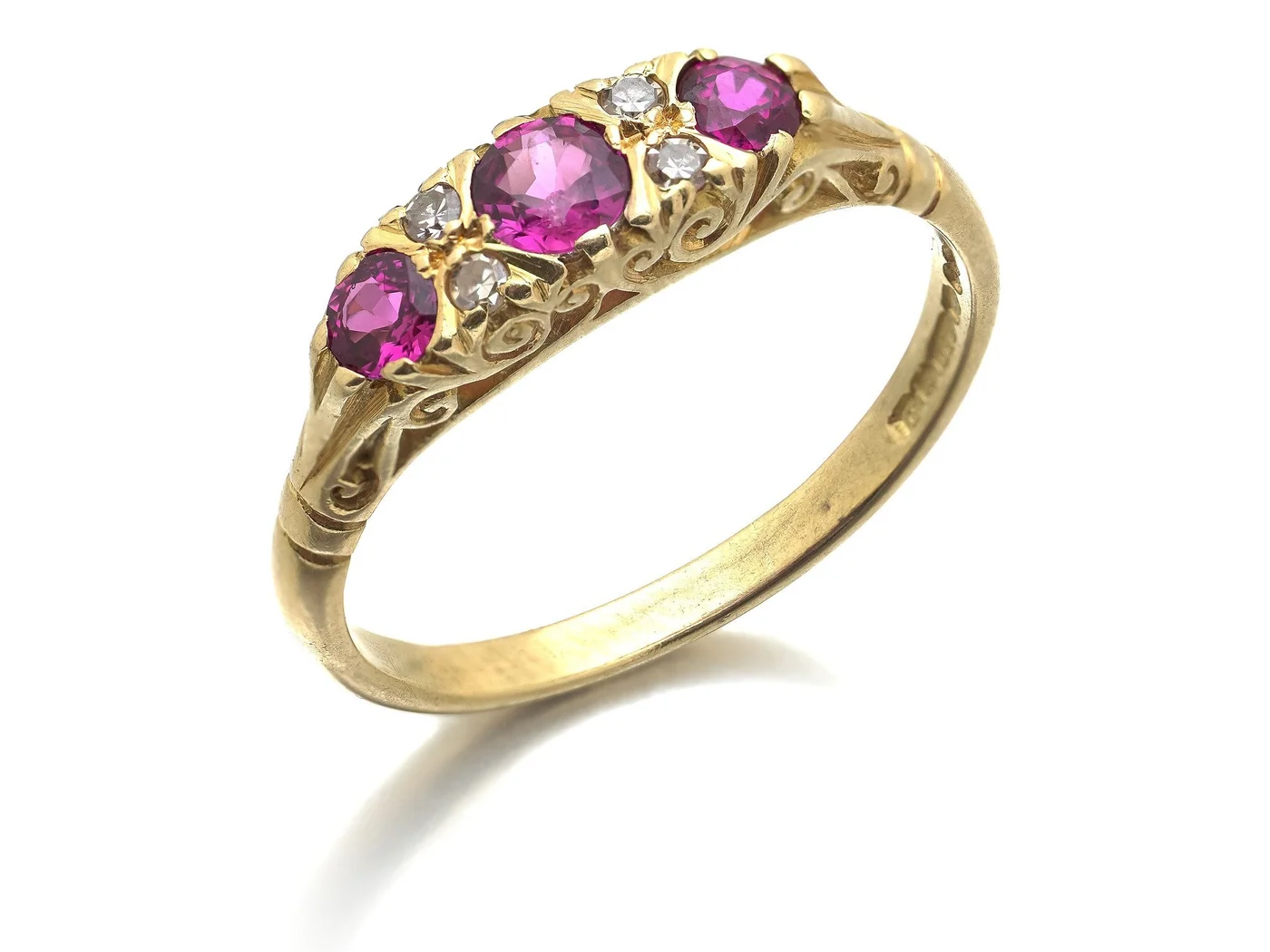 An 18KT gold half hoop ring set with three rubies and four small diamonds in a carved scroll gallery, in the Victorian style