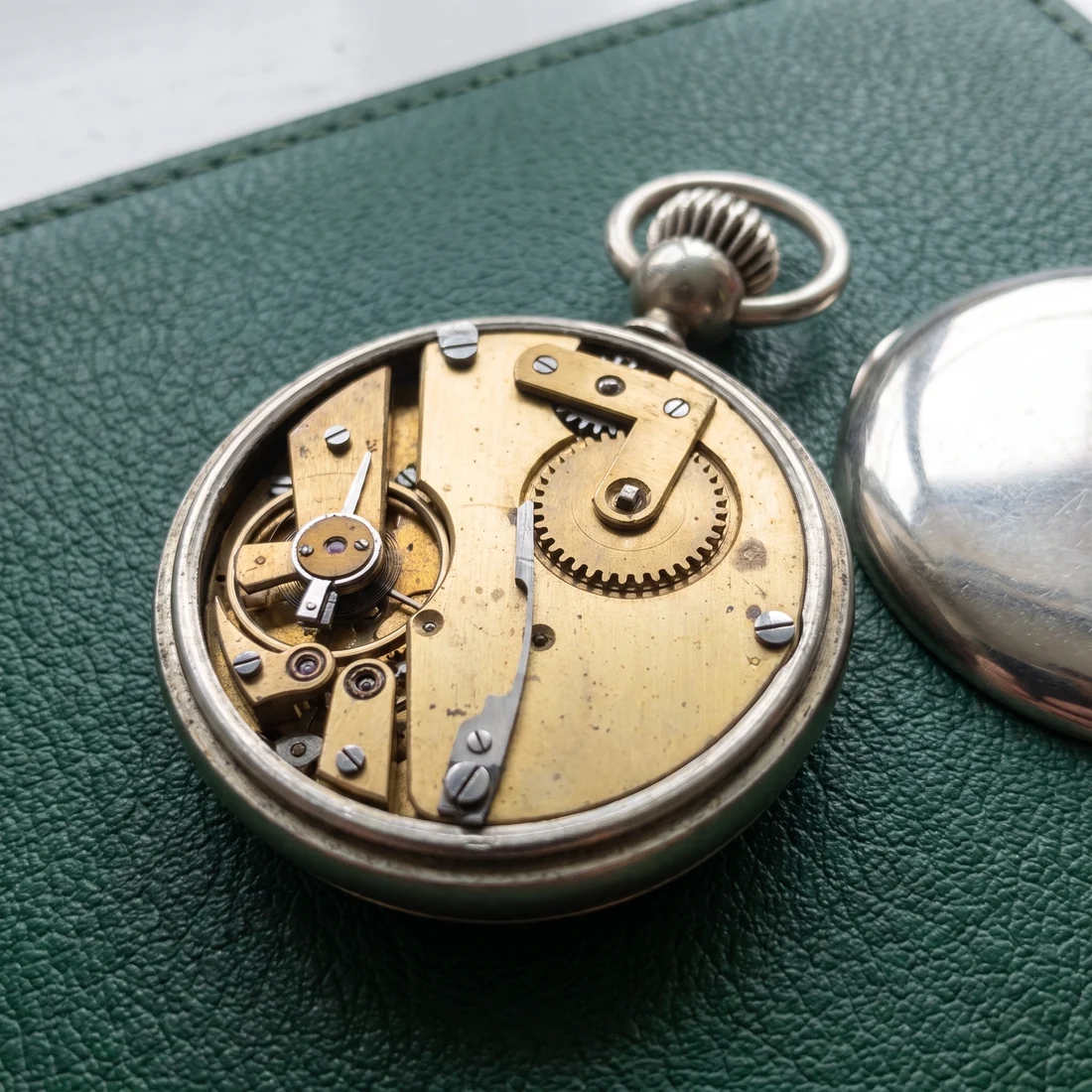 Back removed from a plain chrome pocket watch, showing a simple brass pin-lever movement with steel screws