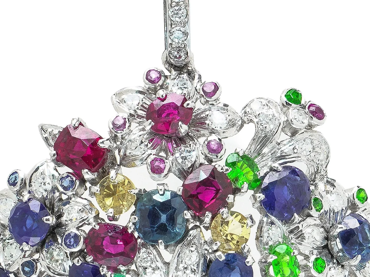 Close-up of a platinum flower basket brooch with rubies, blue, yellow and pink sapphires, emeralds and diamonds set as a bouquet above a band of calibre rubies