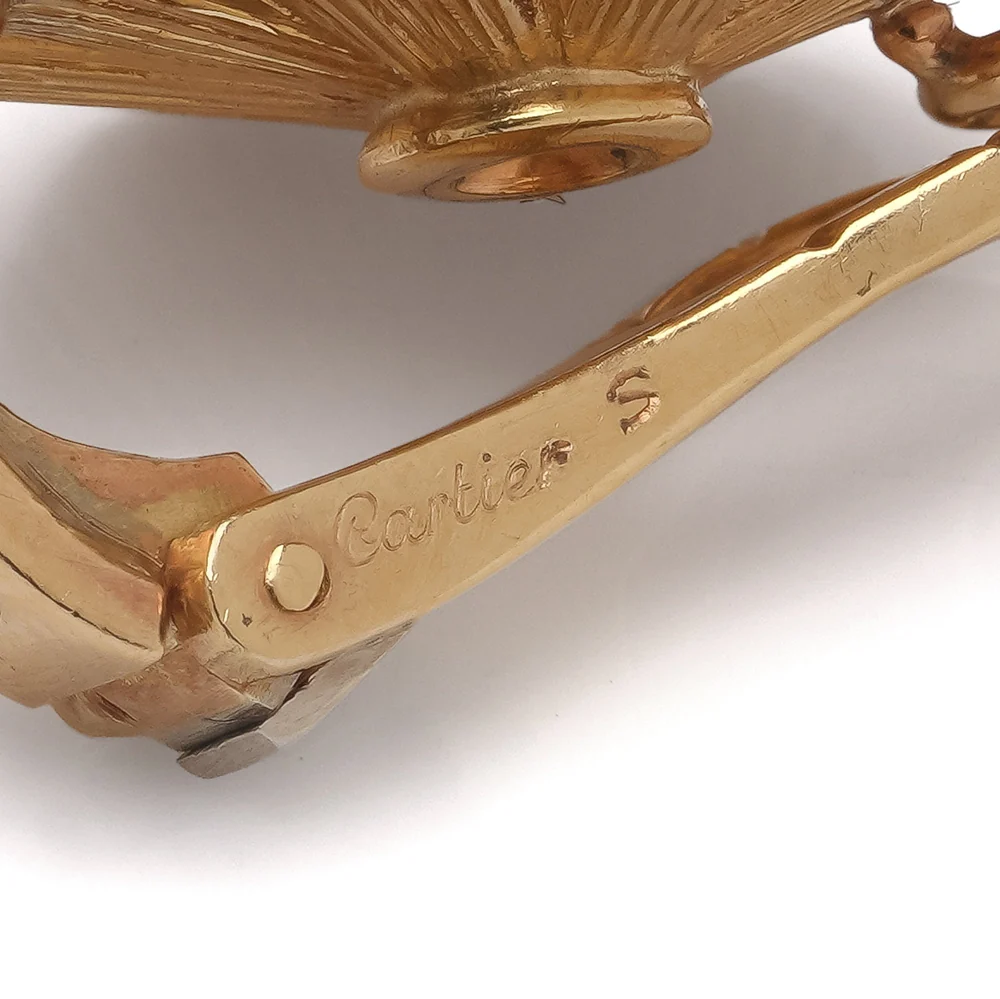Close-up of the gold clip of an earring stamped with the maker's signature in script and a serial letter
