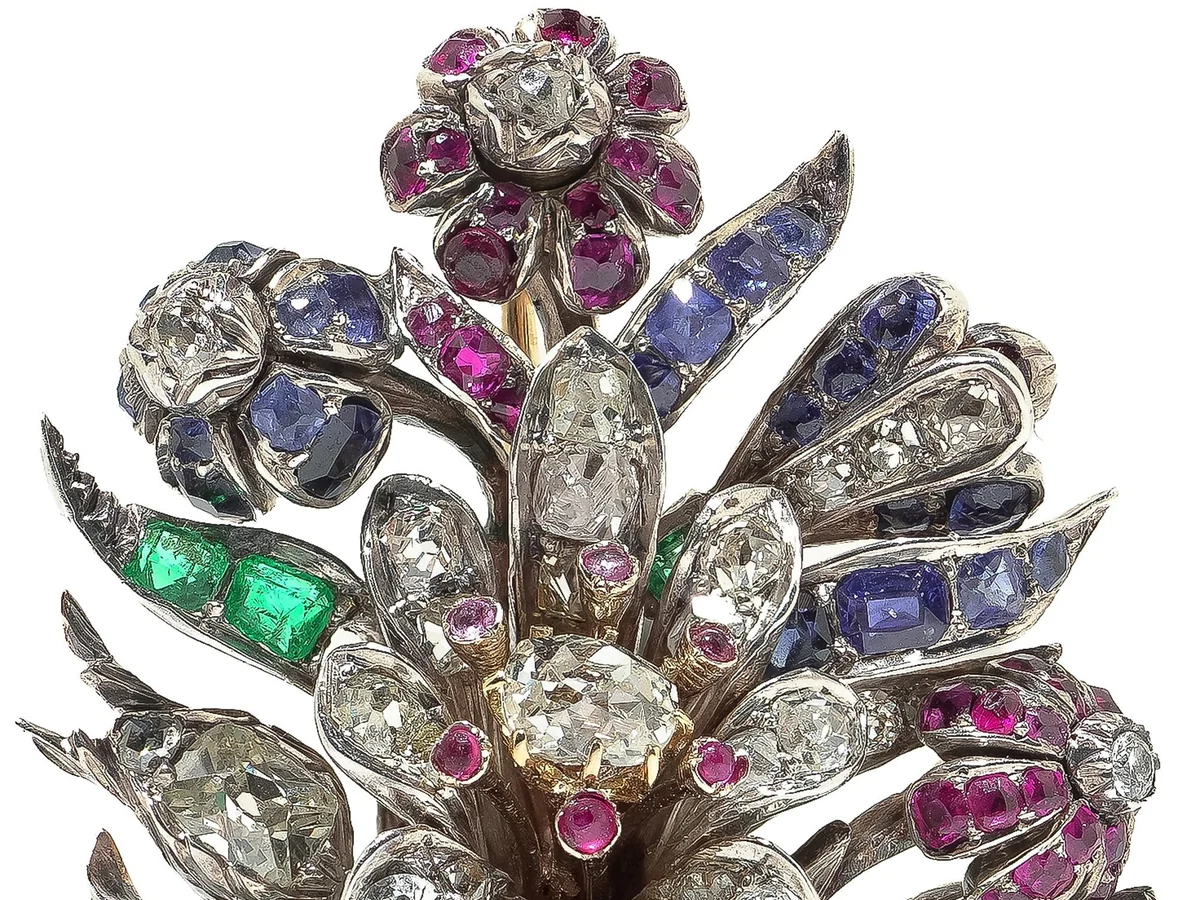 A Victorian flower spray brooch set with old cut diamonds, square emeralds, rubies and blue sapphires in silver, the petals and leaves modelled in relief