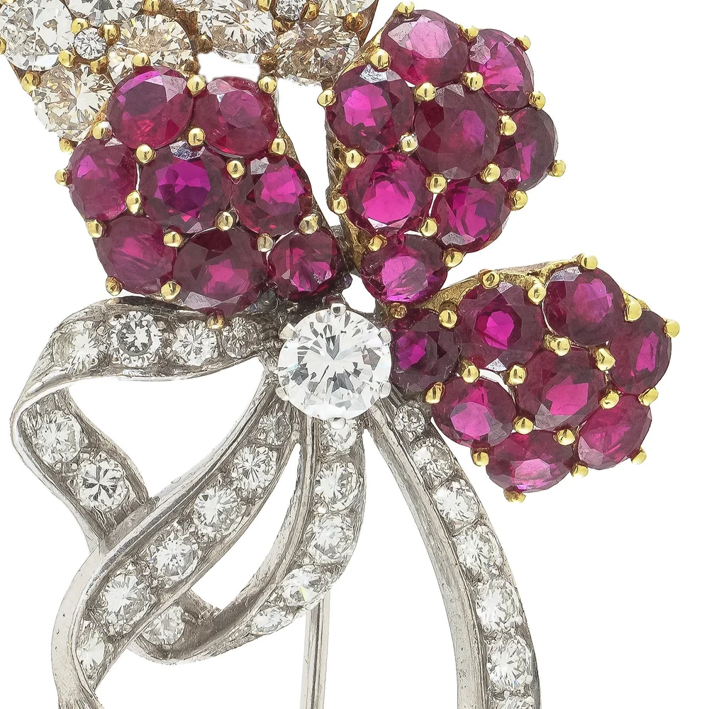 Close-up of a vintage flower brooch with clusters of round rubies in yellow gold claws above curling ribbons pave-set with diamonds in white gold