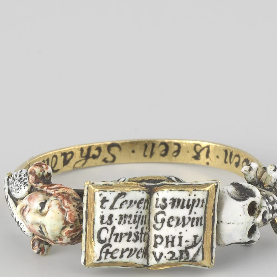 A 17th century enamelled gold memento mori ring with an open book on the bezel, a white skull and crossbones on one shoulder and a winged figure on the other
