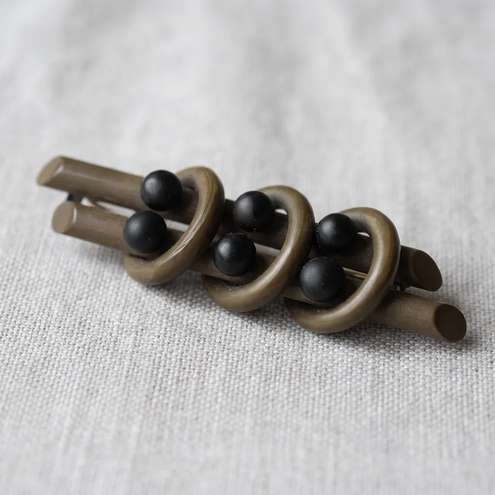 A Victorian bar brooch in moulded vulcanite that has faded to a dull khaki brown, set with round black glass beads that are still deep black